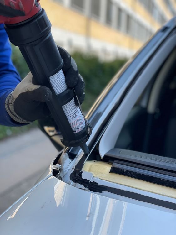 Technicien appliquant la colle pour la pose d’un pare-brise